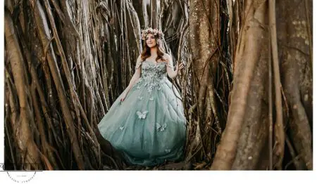 Woman in blue gown standing by tree roots.