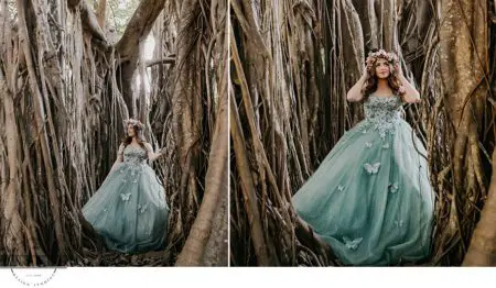 Woman in blue gown stands by tree roots.