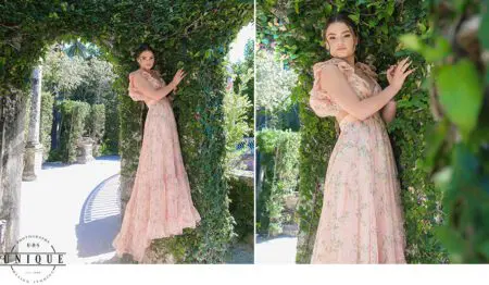 Young woman in a floral dress by a vine-covered wall.