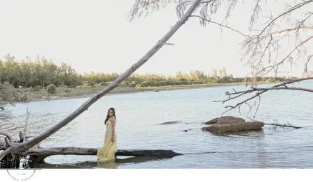 Woman in yellow dress on a log by the water.