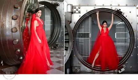 Woman in red dress poses by vault door.