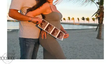 Pregnant couple holding ultrasound on beach.