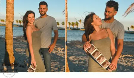 Pregnant couple on beach holding ultrasound photo.
