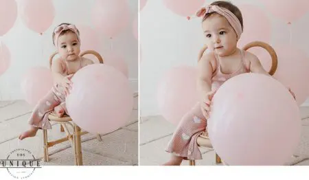 Baby girl in pink outfit with balloons.