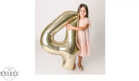 Girl in pink dress holding a gold number 4 balloon.