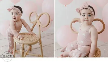 Baby girl in pink sitting on chair with balloons.