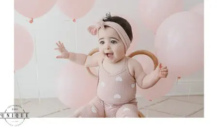 Baby girl in pink outfit with balloons.