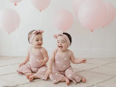 Twin baby girls in pink heart onesies.