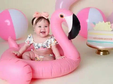 Baby girl in pink flamingo floatie with cake.