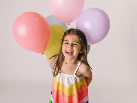 Girl in rainbow dress smiling with balloons.