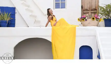 Woman in yellow dress smiling on white wall.
