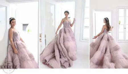 Woman in pink gown poses by window.