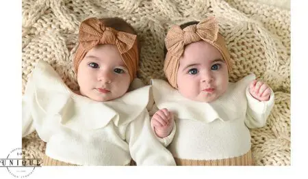 Twin babies in white knit outfits with bows.