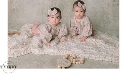 Twin babies in gingham dresses, eight months old.