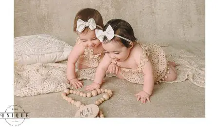 Twin baby girls in white dresses celebrating nine months.