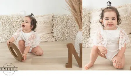 Baby girl in white lace outfit, holding wooden letter O.