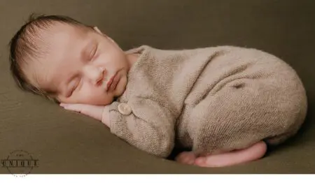 Sleeping newborn baby in a brown onesie.