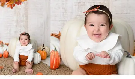 Smiling baby girl with pumpkins and fall leaves.