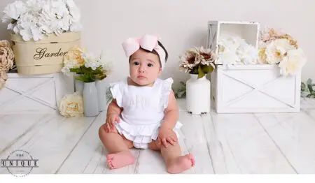 Baby girl in a white dress with a pink bow.