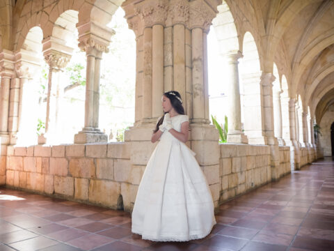 Girl in white dress standing in an arched hallway.