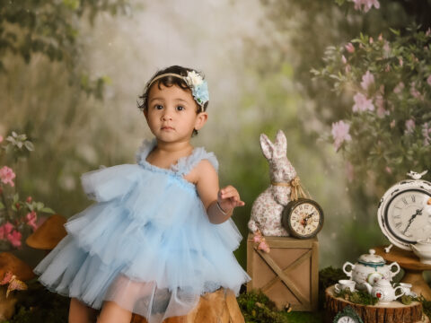 A baby girl in a blue dress in a whimsical setting.